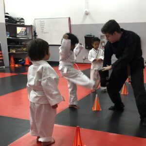 Young child practicing martial arts drills with instructor during a structured confidence-building and coordination-focused training session.