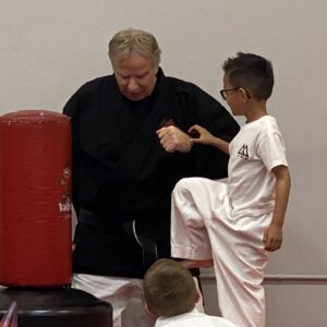 Martial arts instructor guiding student through a kick, showing confidence development through hands-on instruction and repetition