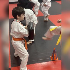 Young martial arts student practicing kick with pad, building confidence through repetition and structured training