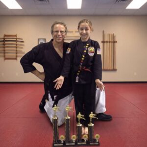 Martial arts instructor and student posing with trophies, showing confidence built through discipline, practice, and achievement